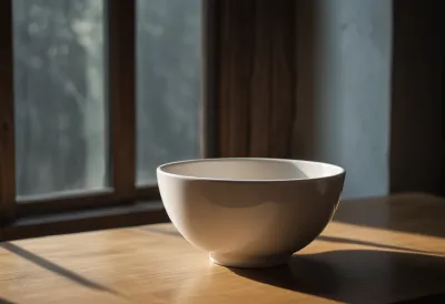 An empty white ceramic bowl on a plain light wooden table.